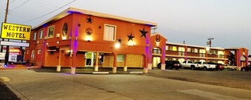 Motel occidental con fachada roja, varias estrellas en el exterior y varios vehículos estacionados al frente.