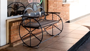 A metal bench outside a building with a brick wall and a window displaying a neon sign. - Western Motel (Shamrock)