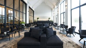 Un vaste espace intérieur comprenant un grand canapé d’angle noir, plusieurs tables et des chaises.