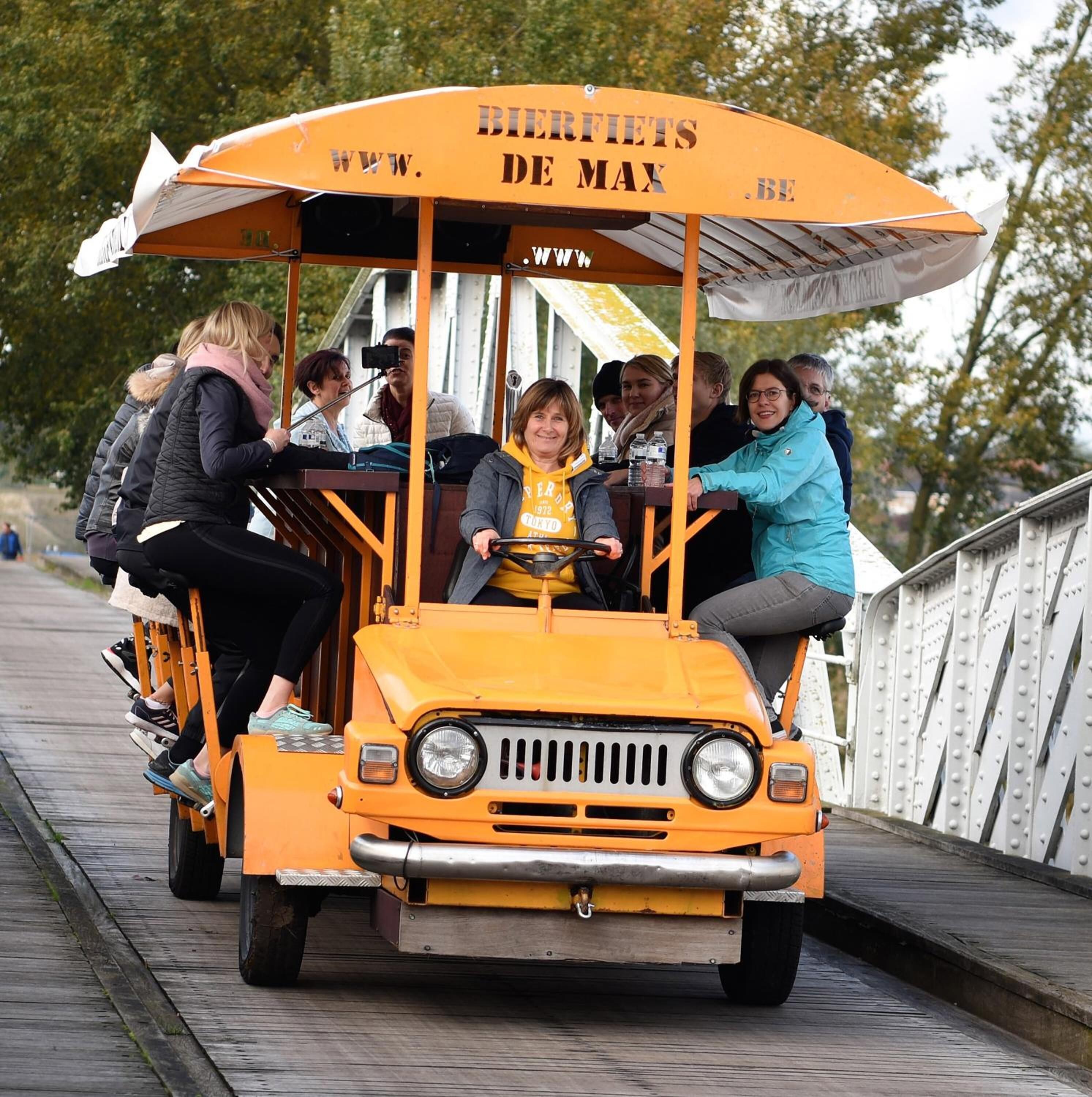 A yellow tram with "BIRFIETS DE MAX" written on the roof, carrying passengers on a bridge.
