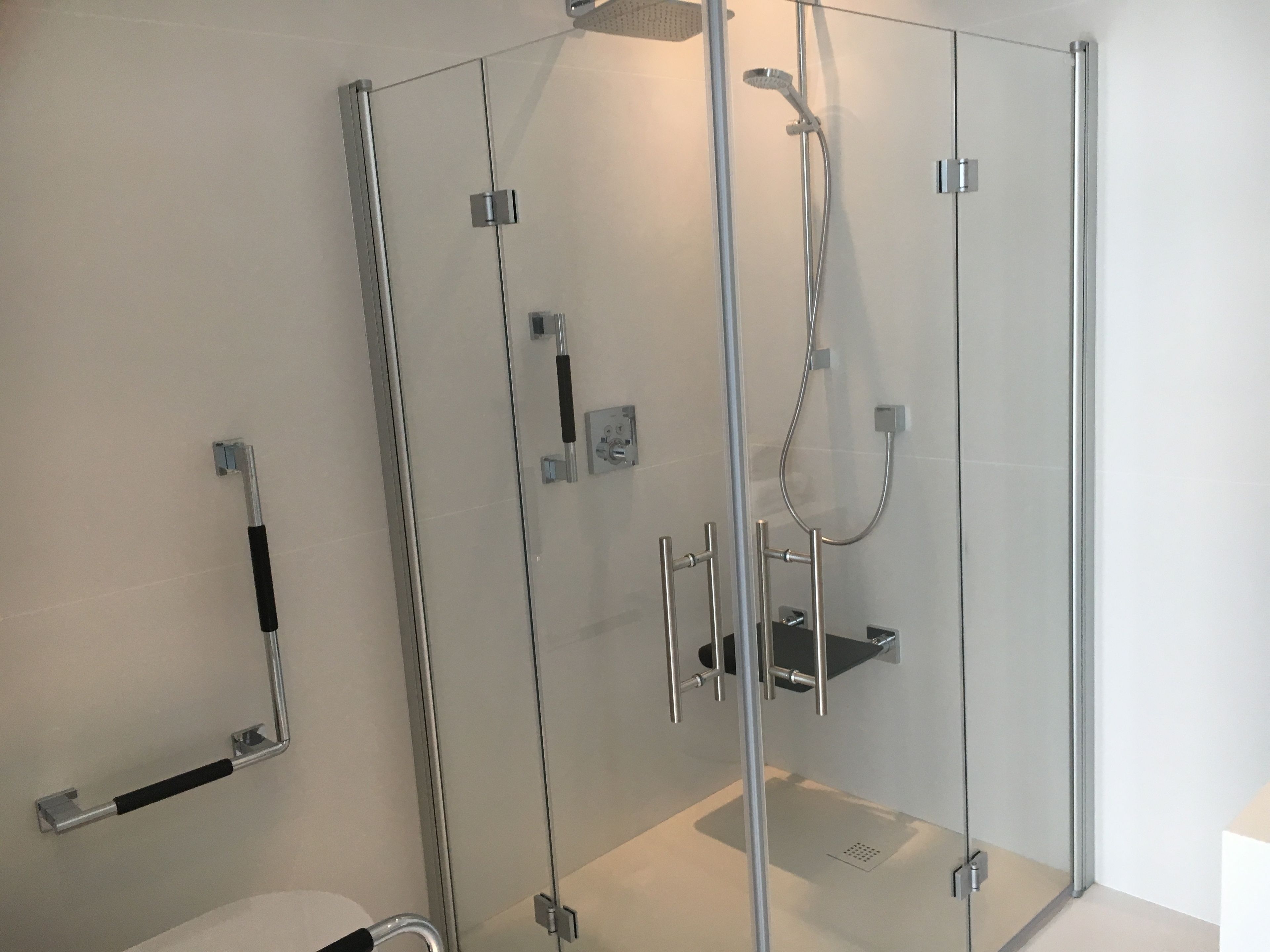 A modern shower enclosure with a glass door, a handheld showerhead, and a wall-mounted control panel.