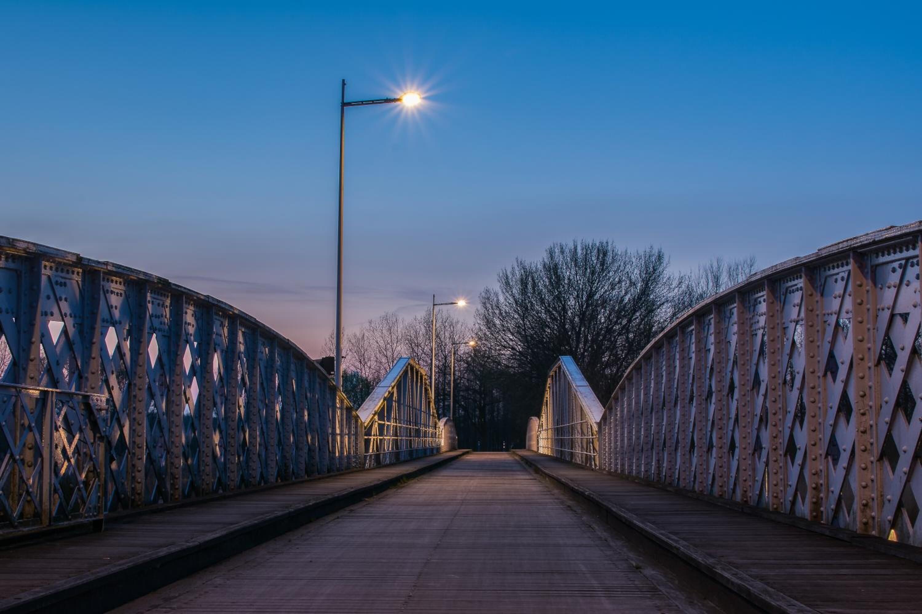 A metal bridge with a wooden walkway and street lamps.