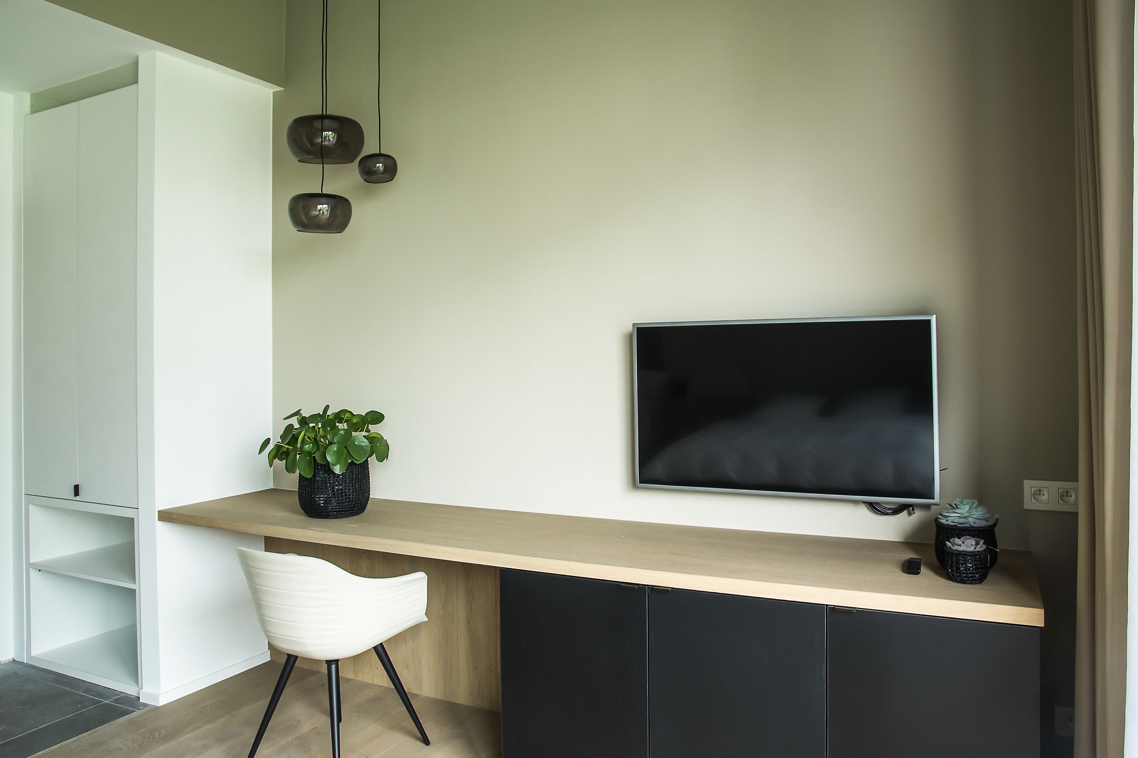 A modern room with a wooden desk, a black TV, a white chair, and a potted plant.