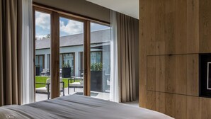 Une chambre moderne avec un grand lit, un téléviseur fixé au mur en bois et une porte-fenêtre coulissante donnant sur une terrasse extérieure.