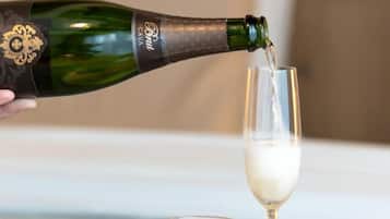 Una bottiglia di champagne che viene versata in un bicchiere, una tazza di caffè, un bicchiere di succo d'arancia e un croissant su un tavolo.
