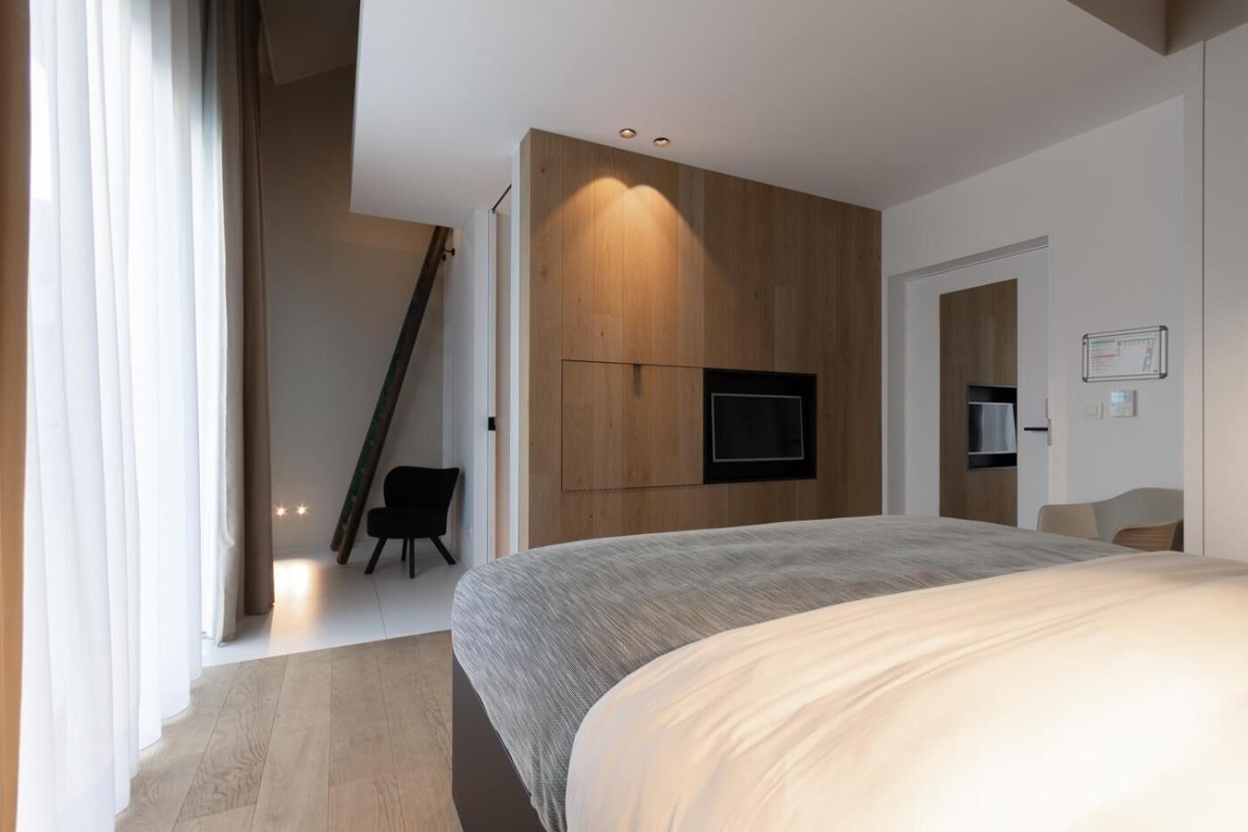 A modern bedroom with a large bed, a TV mounted on the wall, and a staircase leading to another room.