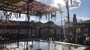 A covered outdoor area with hanging corn cobs, a glass table, and a metal fence. - Hotel Dionisio Inn (Antigua Guatemala)