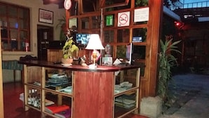 A reception desk with a clock, a plant, and a computer monitor. - Hotel Dionisio Inn (Antigua Guatemala)