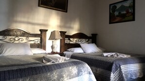 A room with two beds, each with a wooden headboard and white pillows. There is a nightstand with a lamp between the beds. - Hotel Dionisio Inn (Antigua Guatemala)