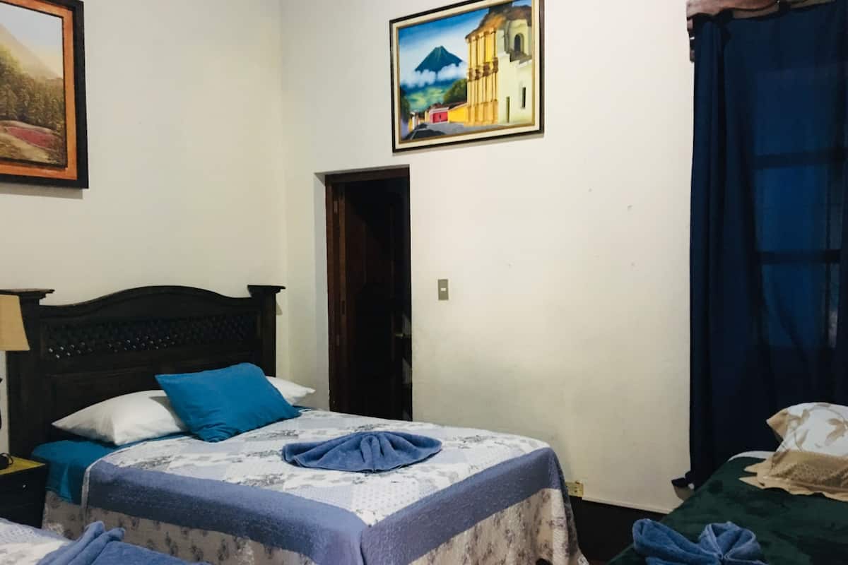 A room with two beds, a wooden headboard, a painting, and a door leading to another room.