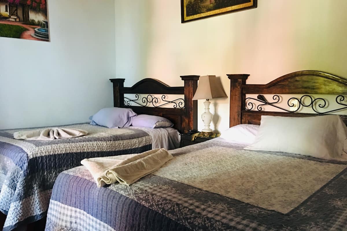 A hotel room with two beds, each with a wooden headboard and a bedside table with a lamp.