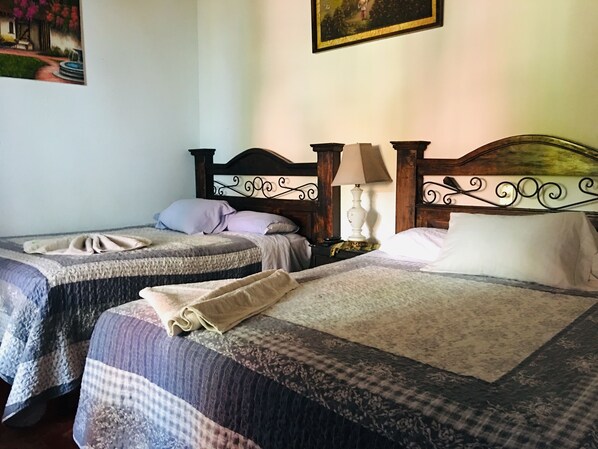 A hotel room with two beds, each with a wooden headboard and a bedside table with a lamp.