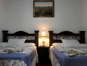 A room with two beds, a nightstand with a lamp, and a painting on the wall.