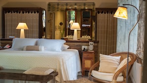 A hotel room with a large bed, two bedside lamps, a wooden nightstand, a wicker chair, and a mirror above the bed. - Toca da Coruja - Eco Luxury Retreat (Tibau do Sul)