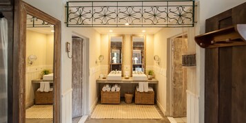 Un baño con dos lavamanos, espejos grandes, cestas de mimbre y una puerta de madera.