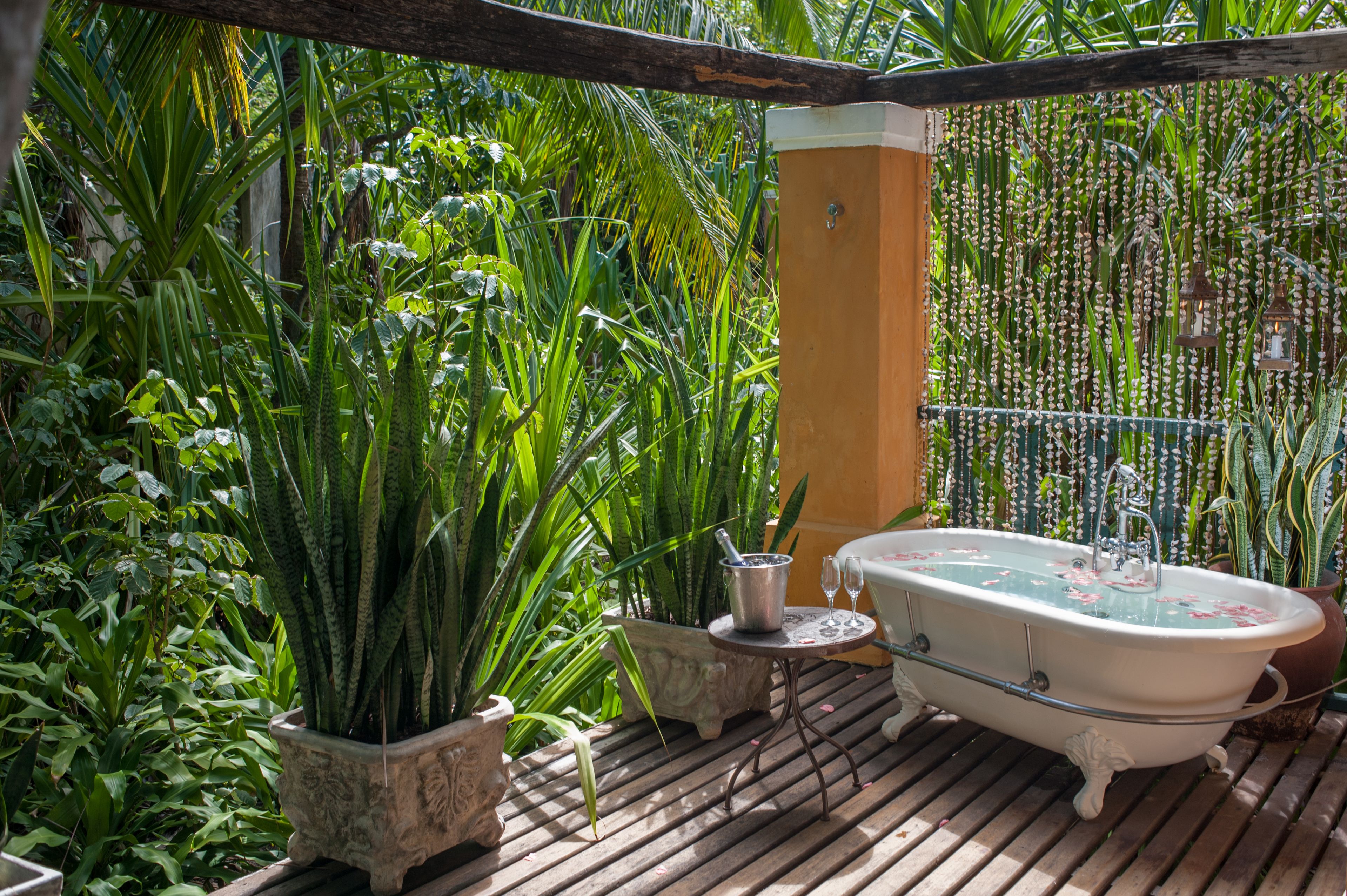 A vintage bathtub on a wooden deck surrounded by lush greenery.