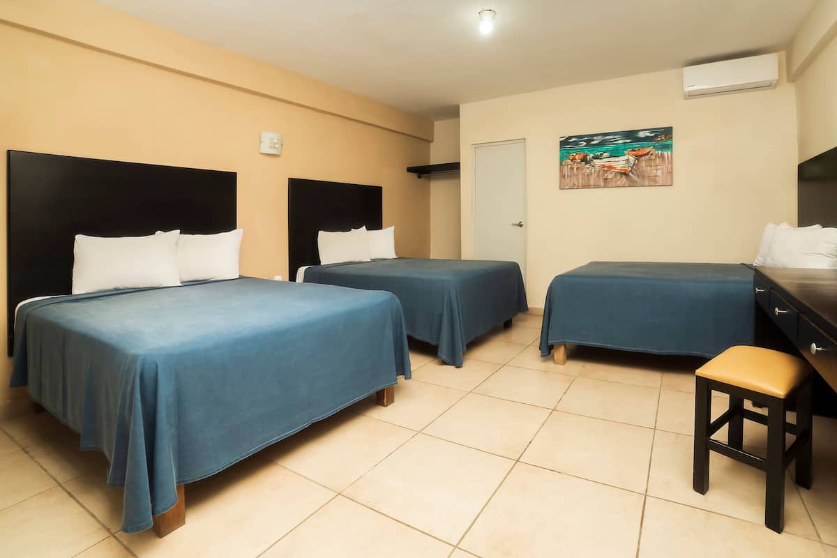 A hotel room with two single beds, a desk, a chair, and an air conditioning unit on the wall.