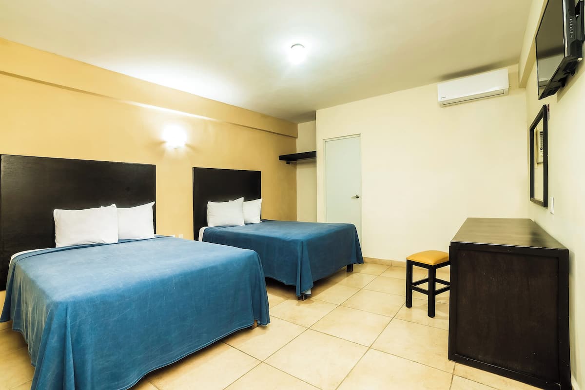 A hotel room with two beds, a small table, a TV, and an air conditioning unit.