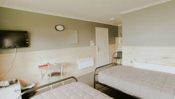 Een kamer met twee bedden, een aan de muur bevestigde televisie, een klein tafeltje met een stoel en een radiator.
