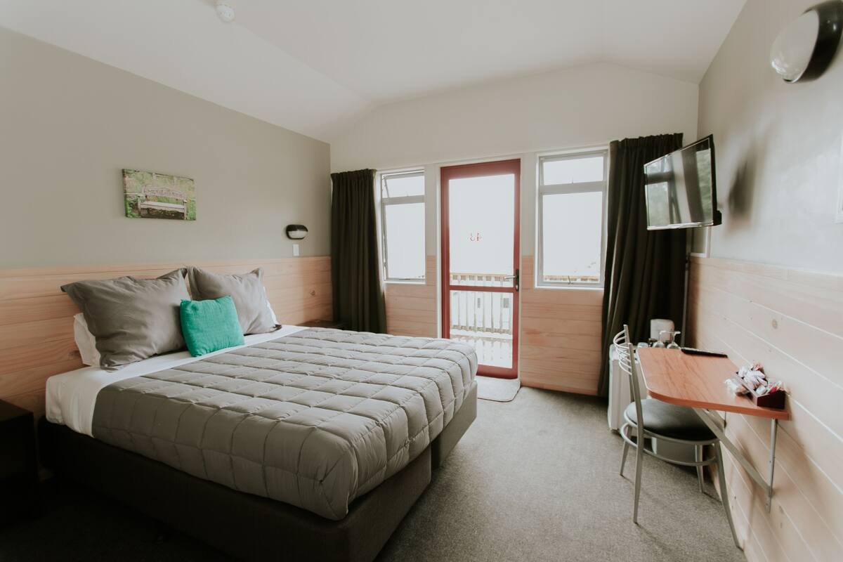 A hotel room with a bed, a desk, a chair, a TV, and a window with curtains.
