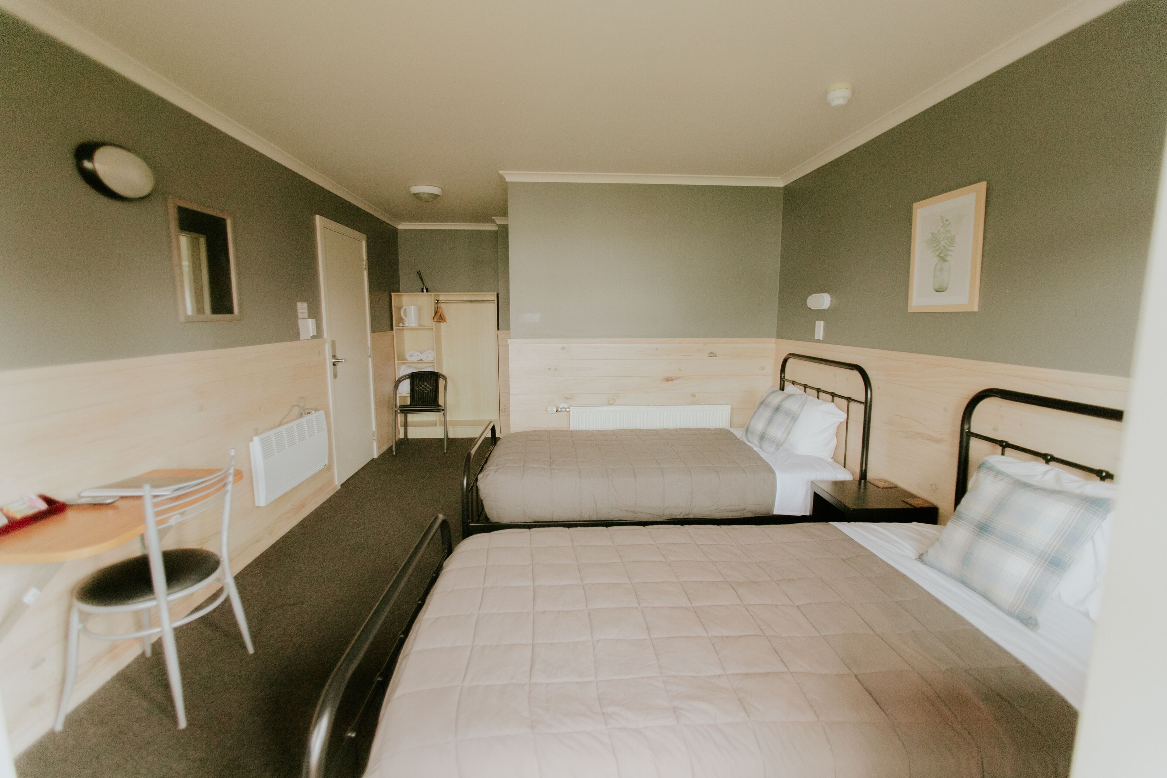 Habitación de hotel con dos camas, una mesita, una silla y un radiador.