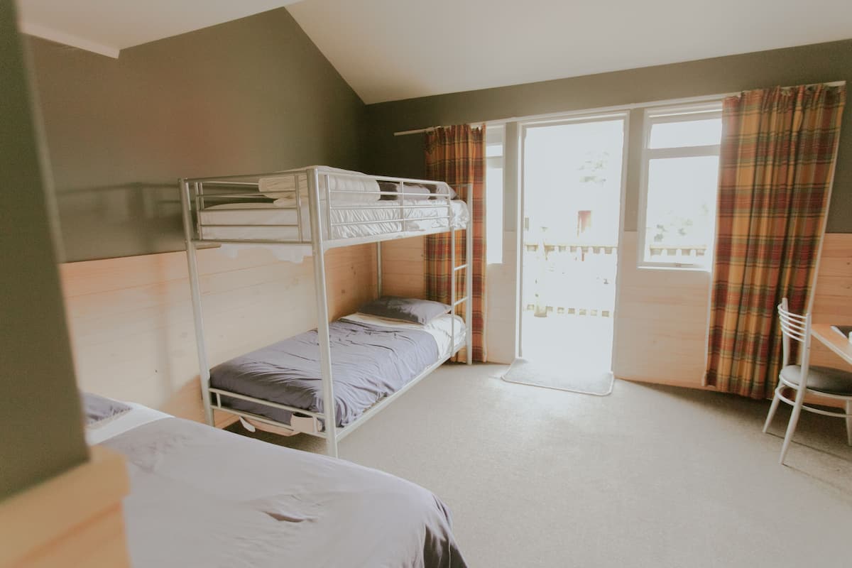 A dormitory room with bunk beds, a desk, and a chair.