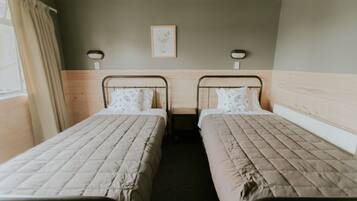A twin room with two single beds, a small bedside table, a framed picture on the wall, and a window with curtains.