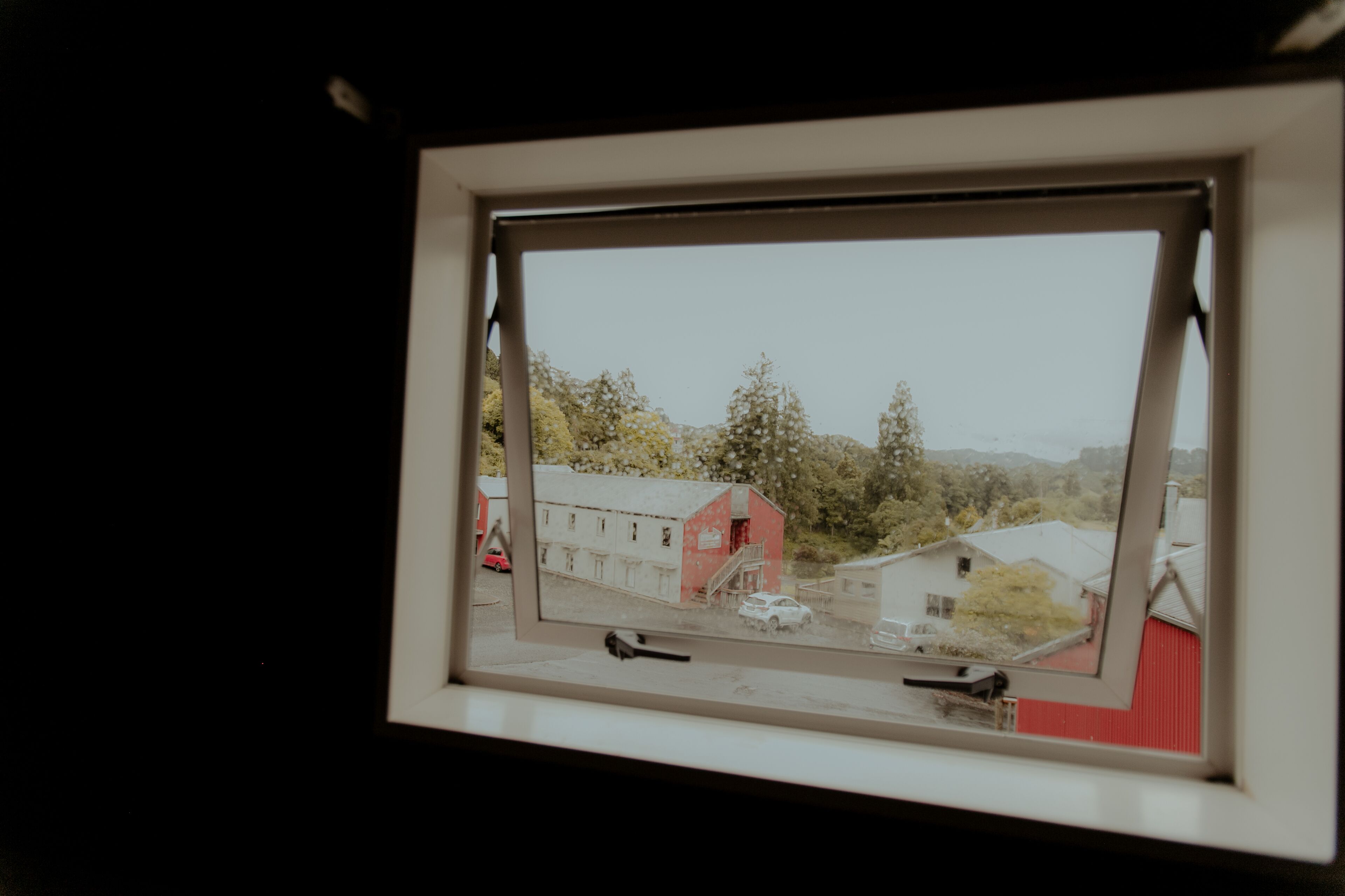 Una ventana con vistas a un edificio rojo y un coche blanco estacionado afuera.