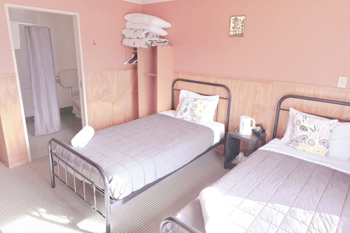 A bedroom with two beds, a wardrobe, a shower area, and a small bedside table with a kettle.