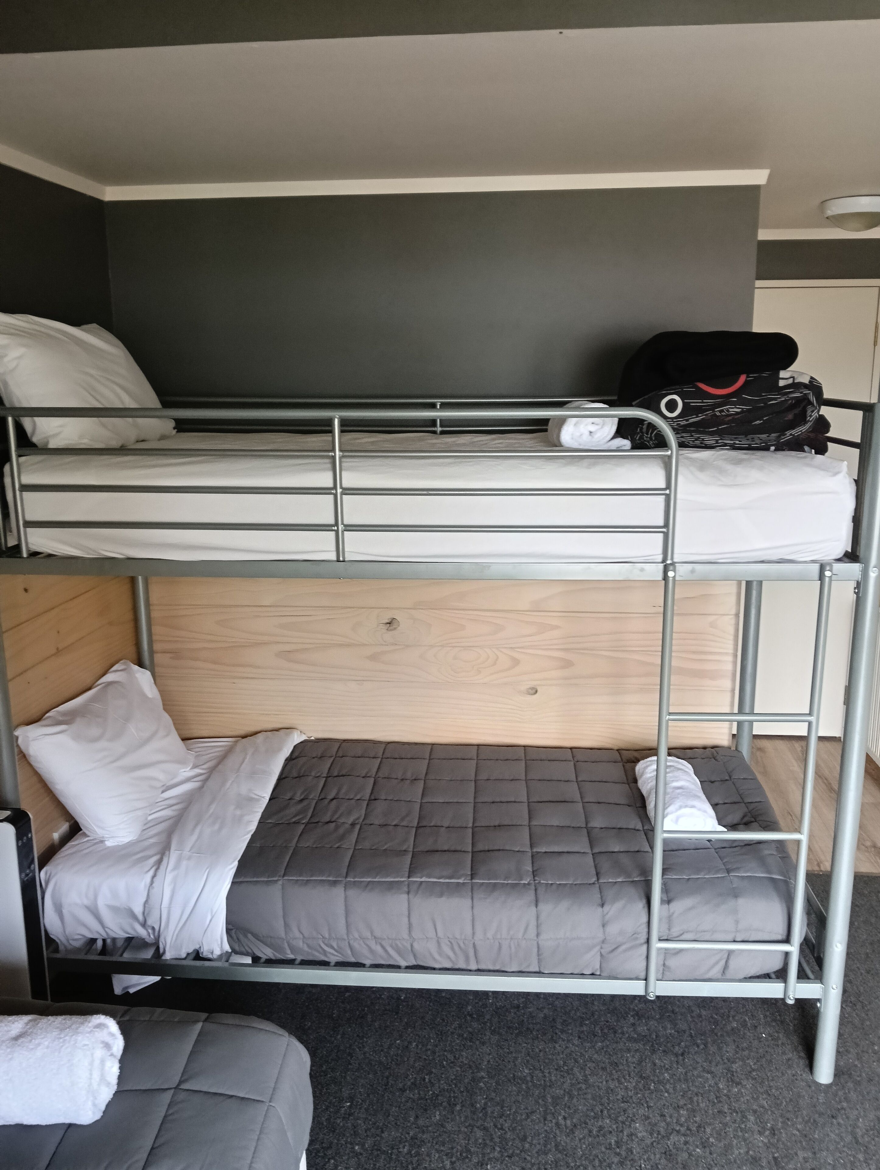 A bunk bed room with a wooden headboard, a grey mattress, and a white pillow.