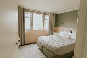 Quarto com cama grande, janela com cortinas, mesa de cabeceira e luminária na parede.