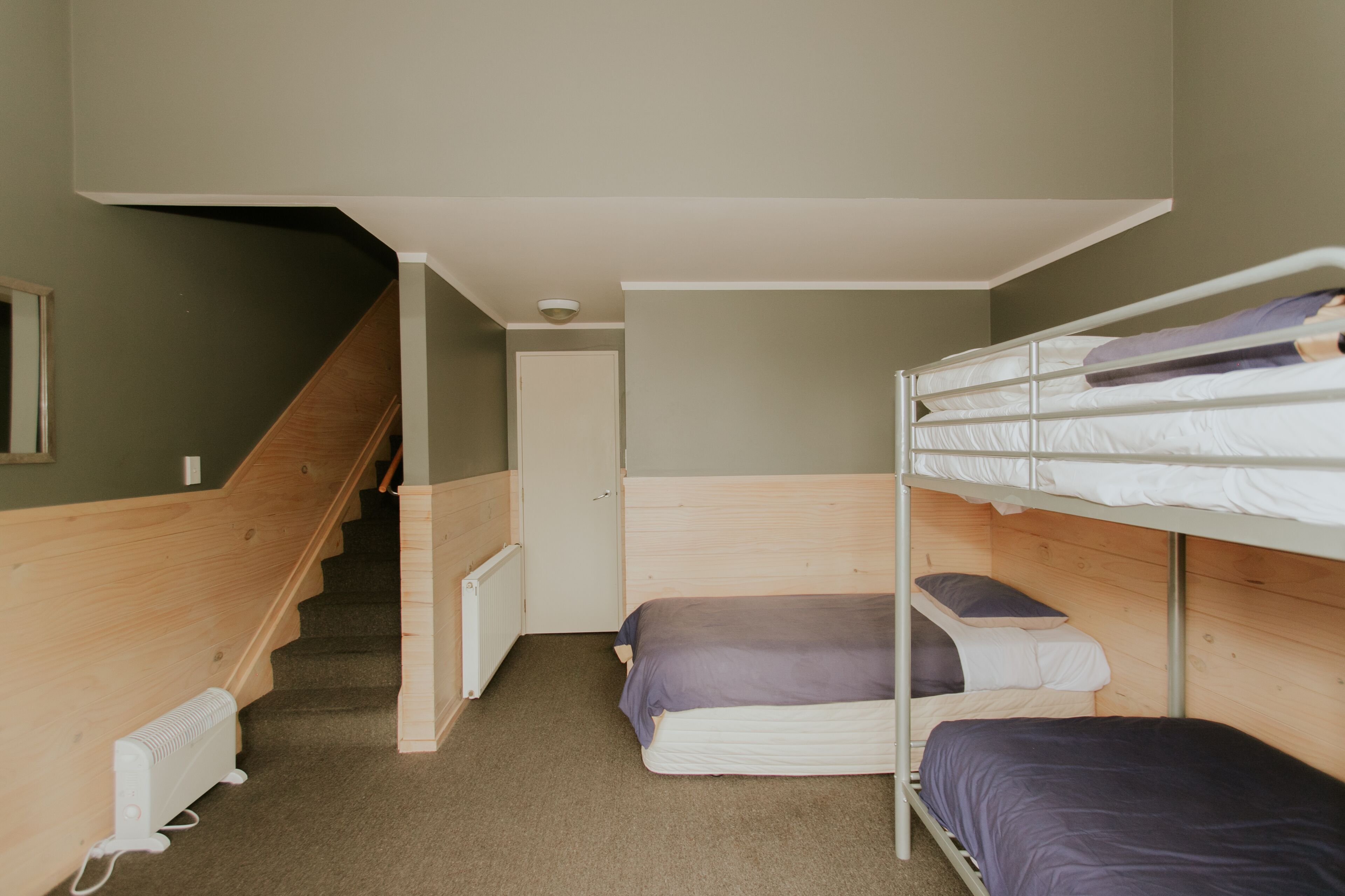A dormitory room with bunk beds, a wooden staircase, and a radiator.