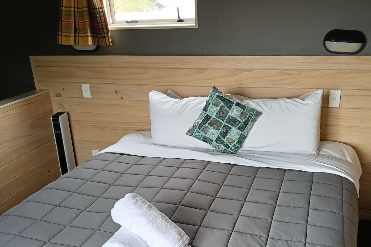 A neatly made bed with a grey quilt, a white pillow, and a green patterned pillow.