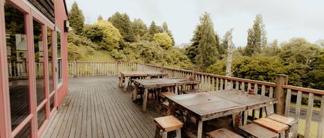 A wooden deck with tables and benches, overlooking a hillside with trees.