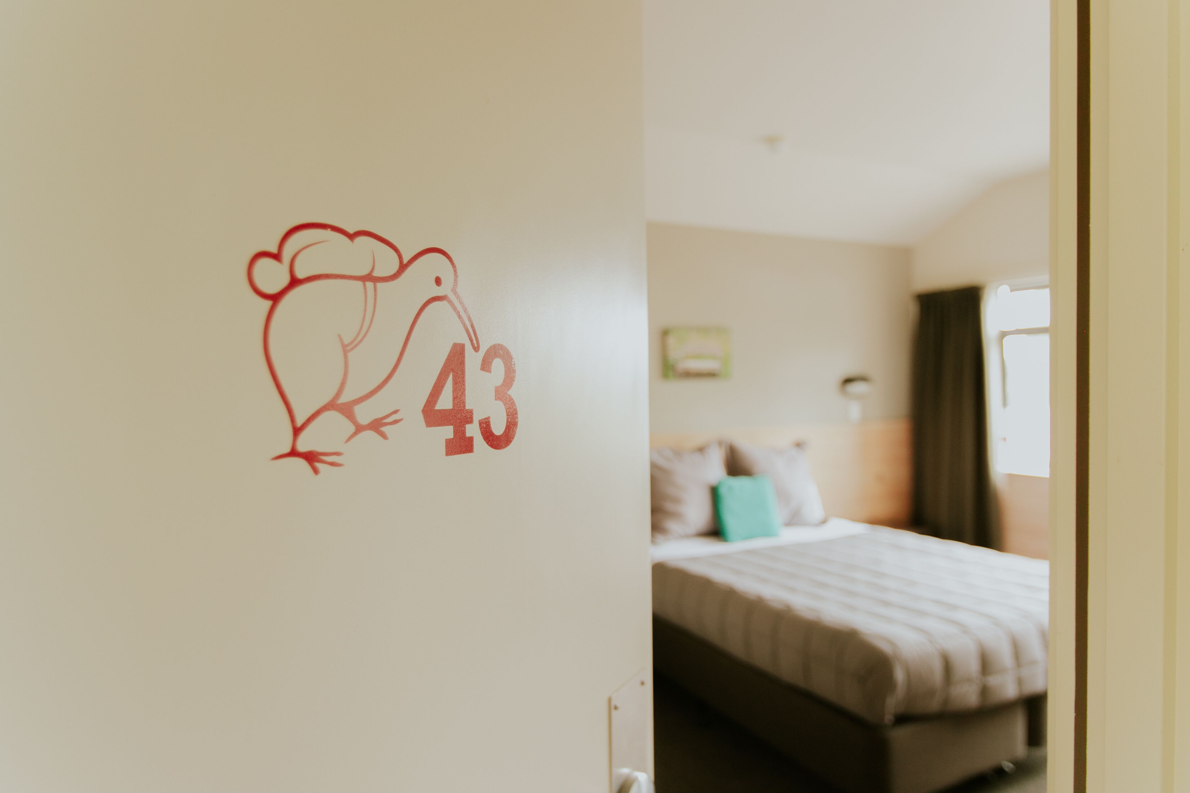 A hotel room with a bed, a wall with a number '43' and a bird drawing, and a window with curtains.