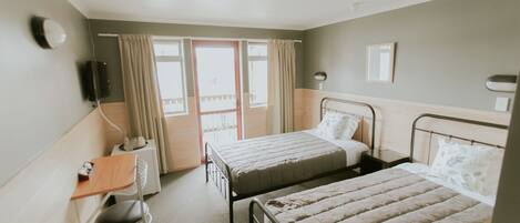 A hotel room with two beds, a desk, a chair, a bedside table, a lamp, and a window with curtains.
