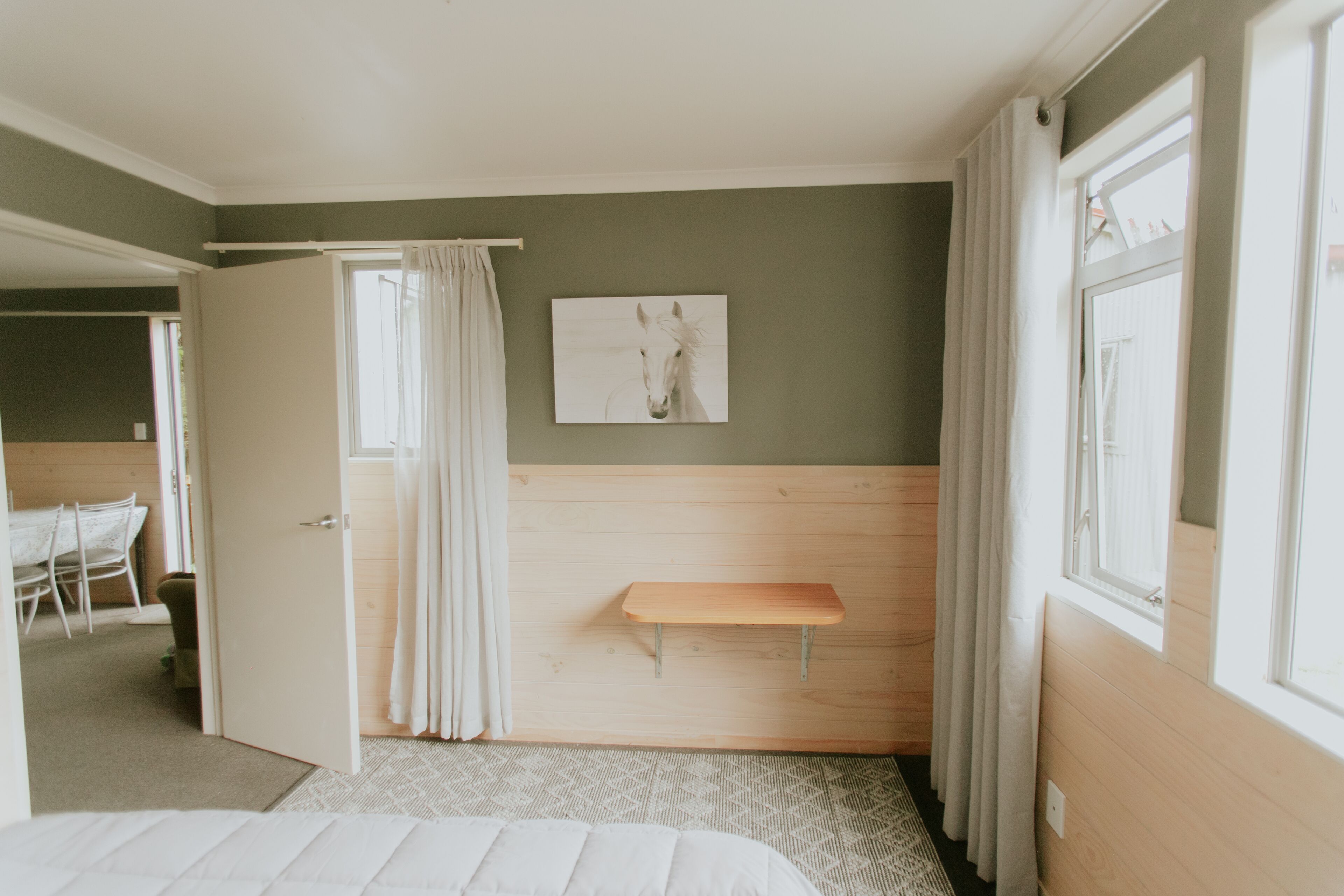 Un dormitorio con cama, un banco de madera, un cuadro en la pared y una ventana con cortinas.