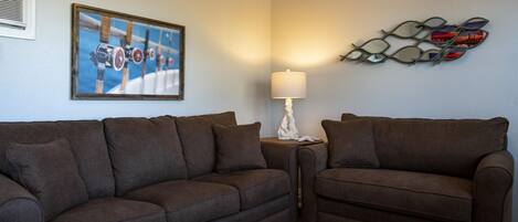 A living room with two brown sofas, a framed picture of a boat, a wall-mounted lamp, and a decorative mirror.