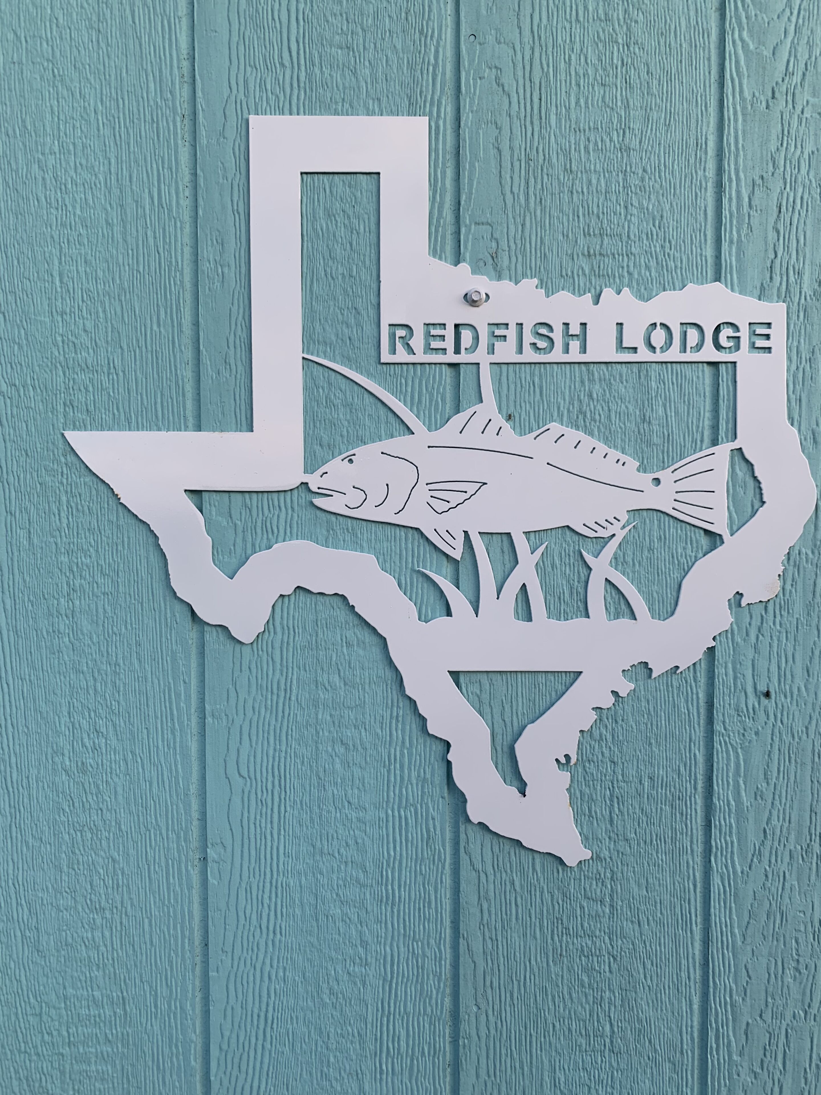 A cut-out of the Texas state outline with a fish and the text "Redfish Lodge" on a teal wooden background.