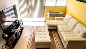 A living room with a piano, a sectional sofa, and a large window with blinds.