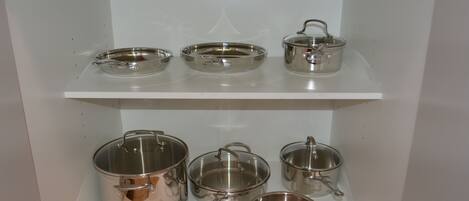 Een keuken met roestvrijstalen pannen en keukengerei op planken.