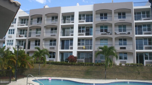 A multi-story hotel with balconies, a swimming pool, and palm trees.