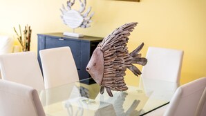 A dining table with a unique wooden fish sculpture centerpiece, surrounded by white chairs.