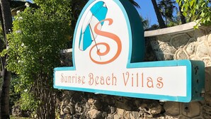 Une enseigne pour le complexe hÎtelier Sunrise Beach Villas, avec un logo stylisé en forme de « S » et un palmier.