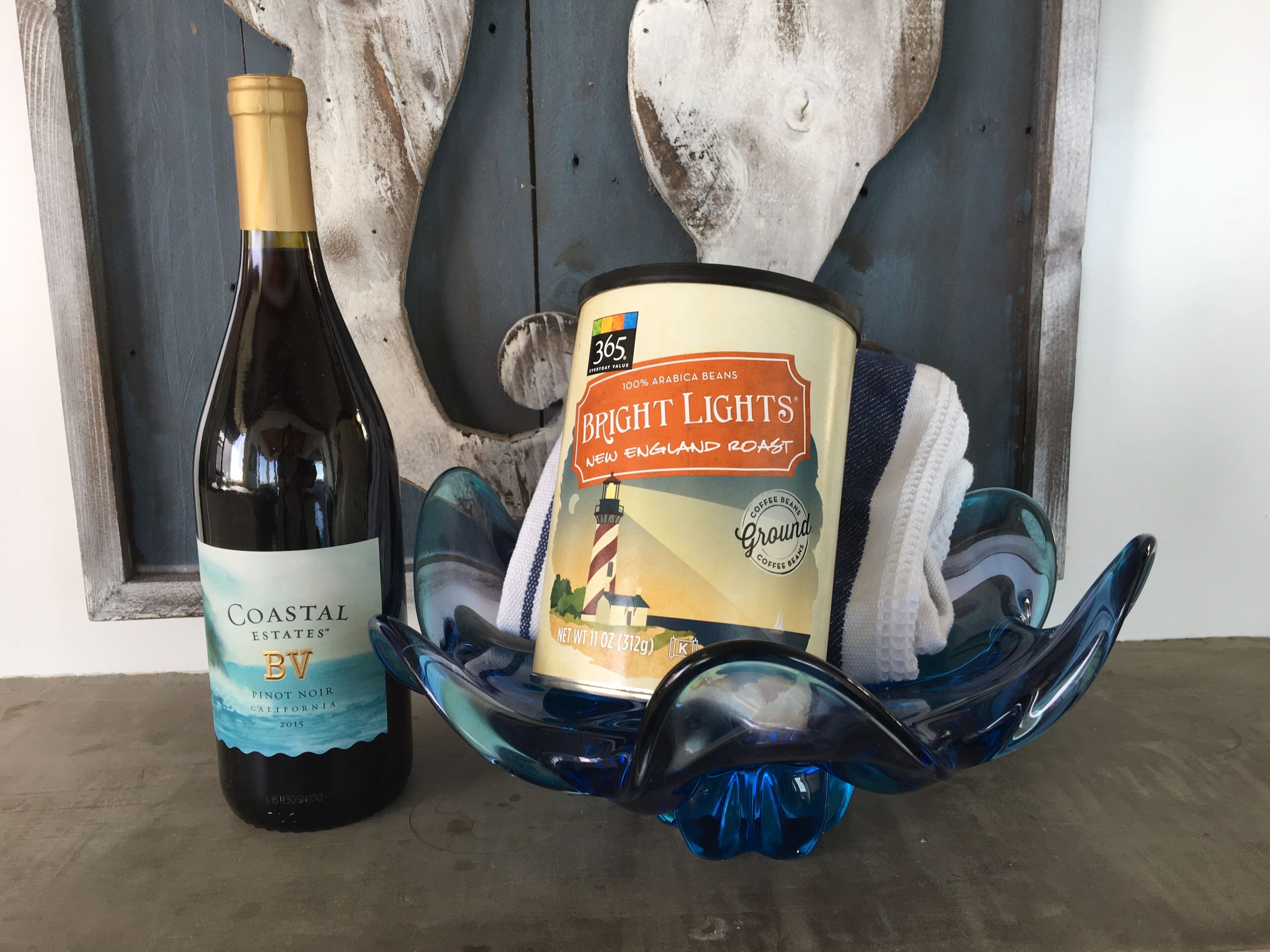 A bottle of Coastal Estates BV Pinot Noir and a can of Bright Lights New England Roast coffee beans on a blue glass dish.