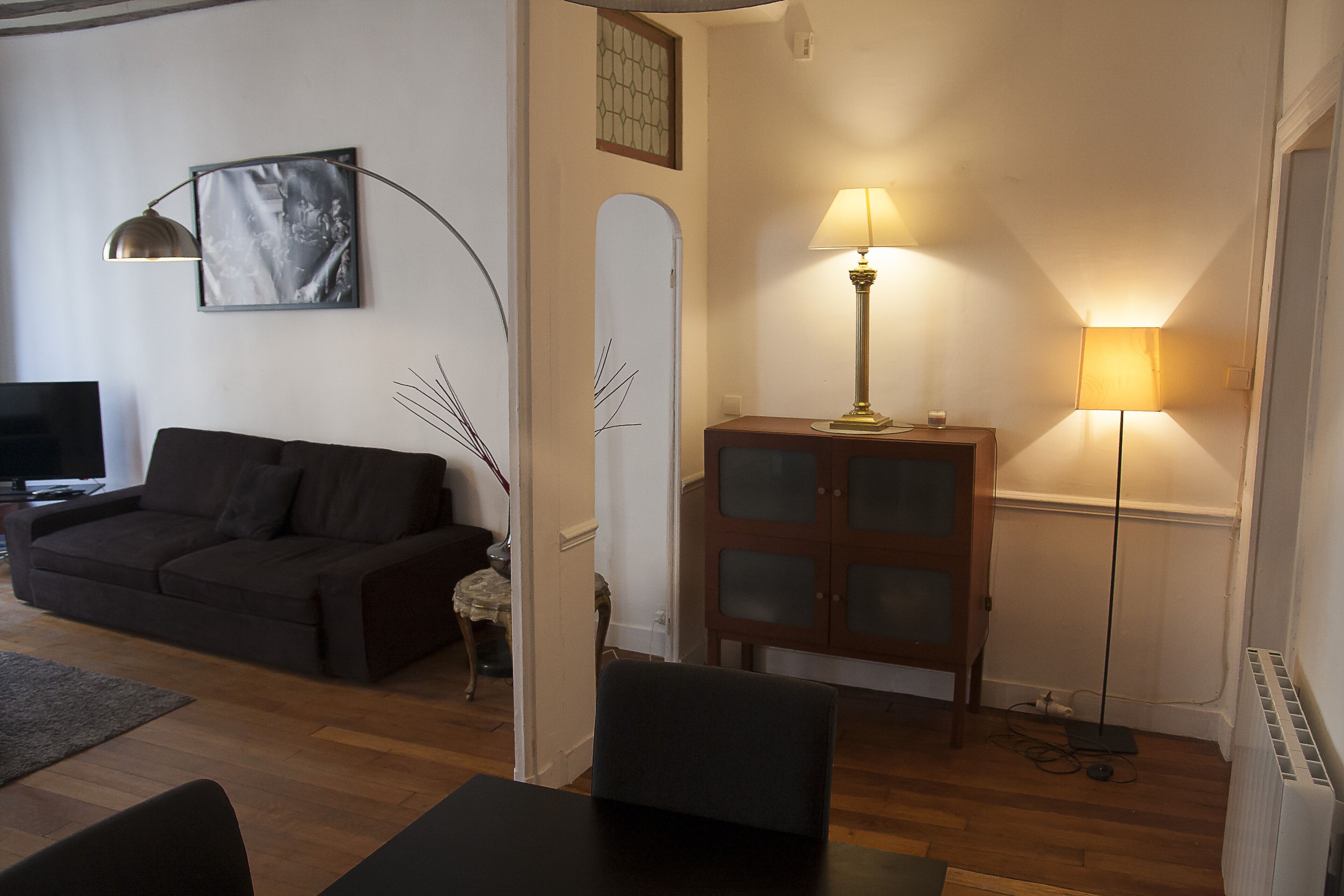 A living room with a dark-colored sofa, a small table, a cabinet with glass doors, and two floor lamps.