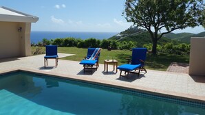 A pool area with three blue lounge chairs, a small table, and a view of the ocean. - East End Overlook, 3 Acre Ridgetop Estate with Dual Shore Views (Saint Croix)