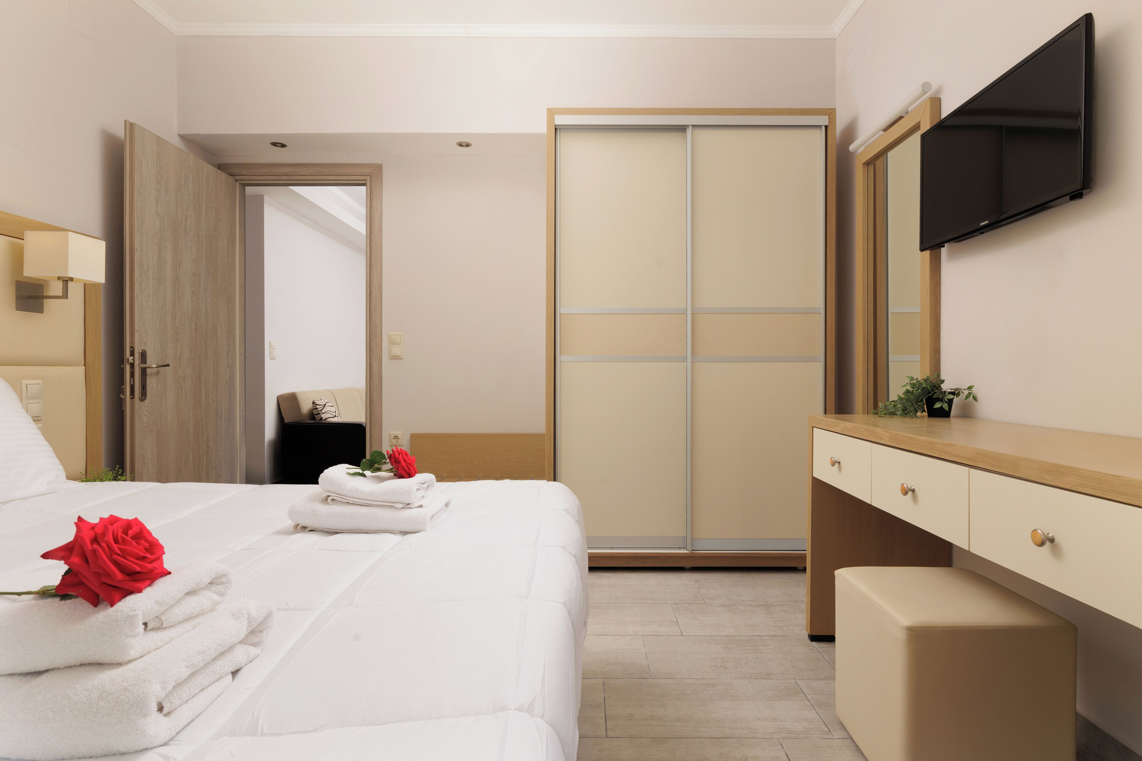 Een hotelkamer met een bed, een houten garderobe, een aan de muur bevestigde televisie en een nachtkastje met een lamp.