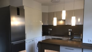 Eine moderne Küche mit Einbaukühlschrank, Waschmaschine, Toaster und Kaffeemaschine. Ein Holztisch mit Stühlen steht daneben.