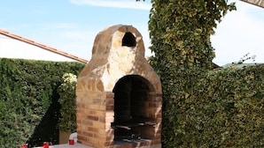 Ein Backofen aus Ziegelsteinen im Freien, mit einem Tisch und Stühlen in der Nähe.